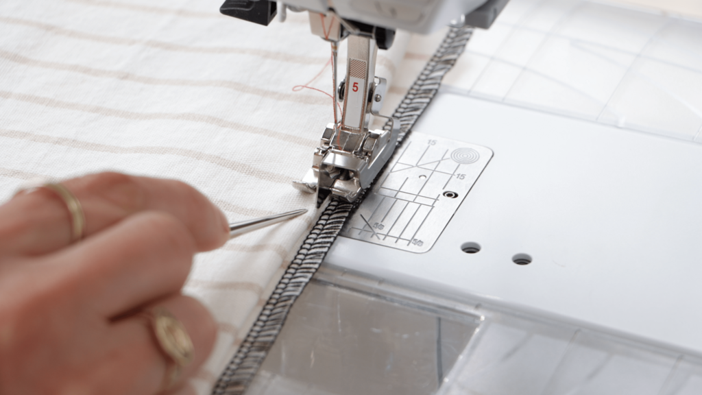 hands positioning the folded fabric under the blind hem foot, showing the three-layer setup