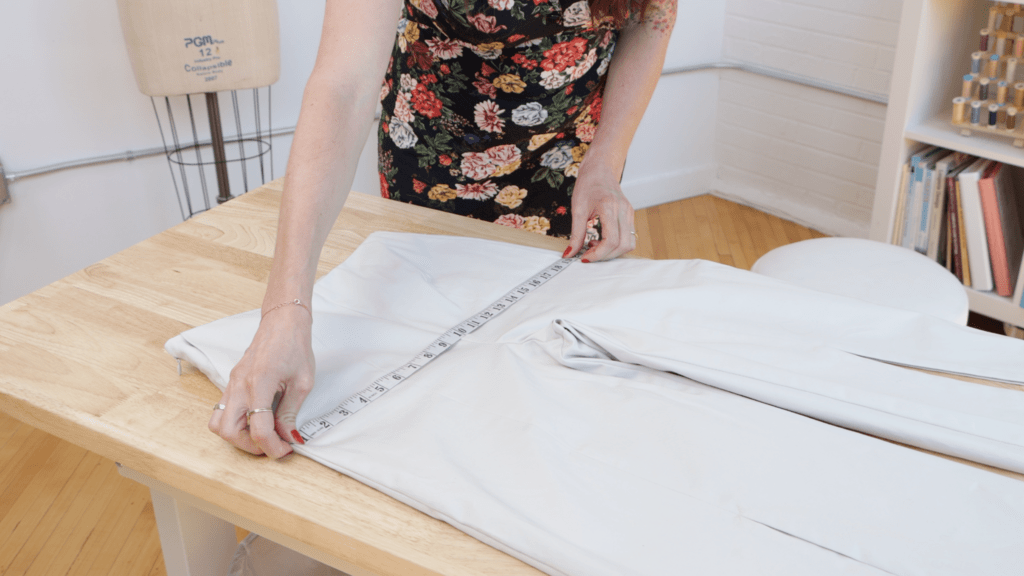 hands measuring a pair of jeans laid flat, with measuring tape across the waist