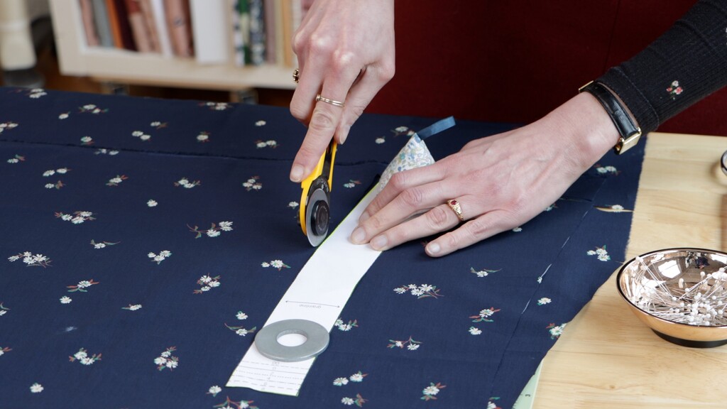 hands using a rotary cutter to smoothly cut along a pattern edge held down by pattern weights