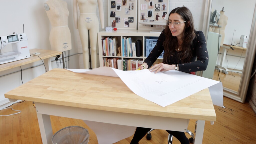frustrated sewist trying to manage large sheets of pattern paper that are sliding off a cutting table