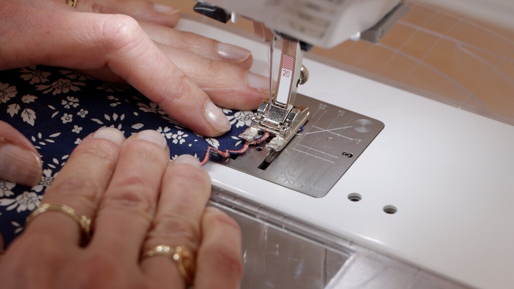Close-up of the zigzag encasing pass being stitched, showing how the stitch swings off the trimmed edge