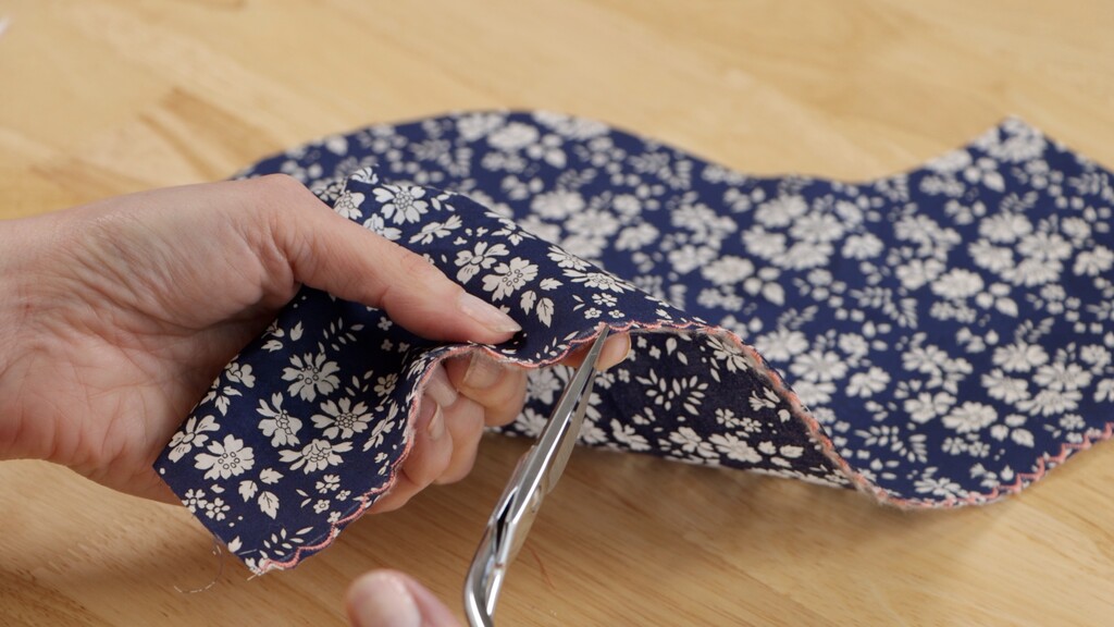 Hands trimming close to scallop stitching with small embroidery scissors, showing the precise trim needed
