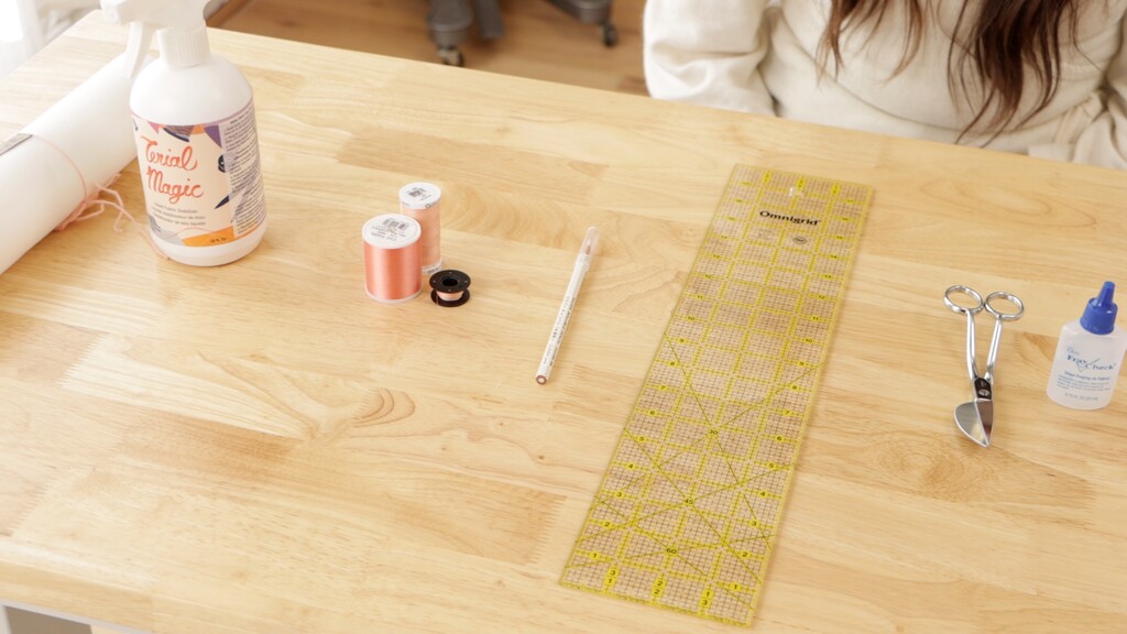 Flat lay of all materials — stabilizer, spray starch, rayon embroidery thread, fabric marker, seam sealant, and embroidery scissors arranged neatly
