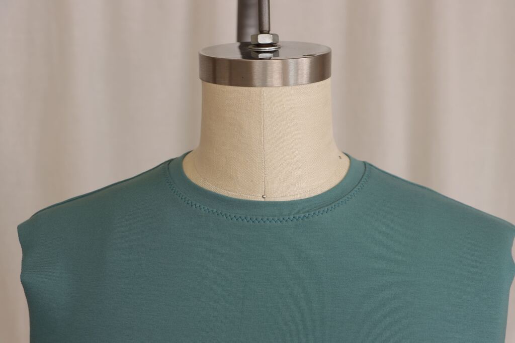 Finished neckband on a completed knit top, showing clean, even topstitching lying flat against the garment