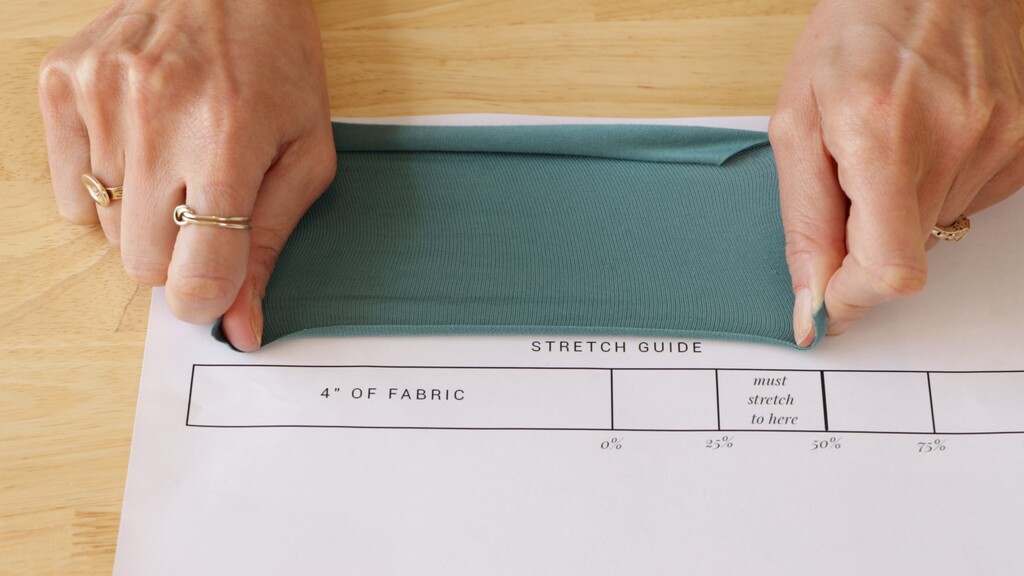 Hands stretching a piece of knit fabric across a ruler to demonstrate measuring stretch percentage
