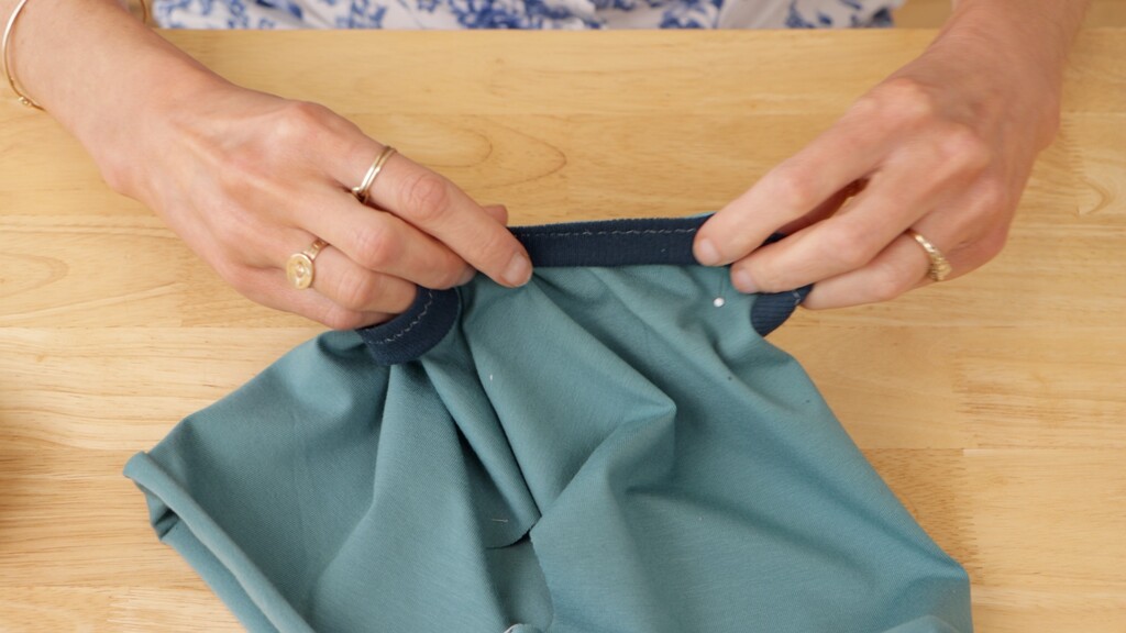 Hands pinning a neckband to a neckline, showing the band being stretched evenly as pins are placed around the curve