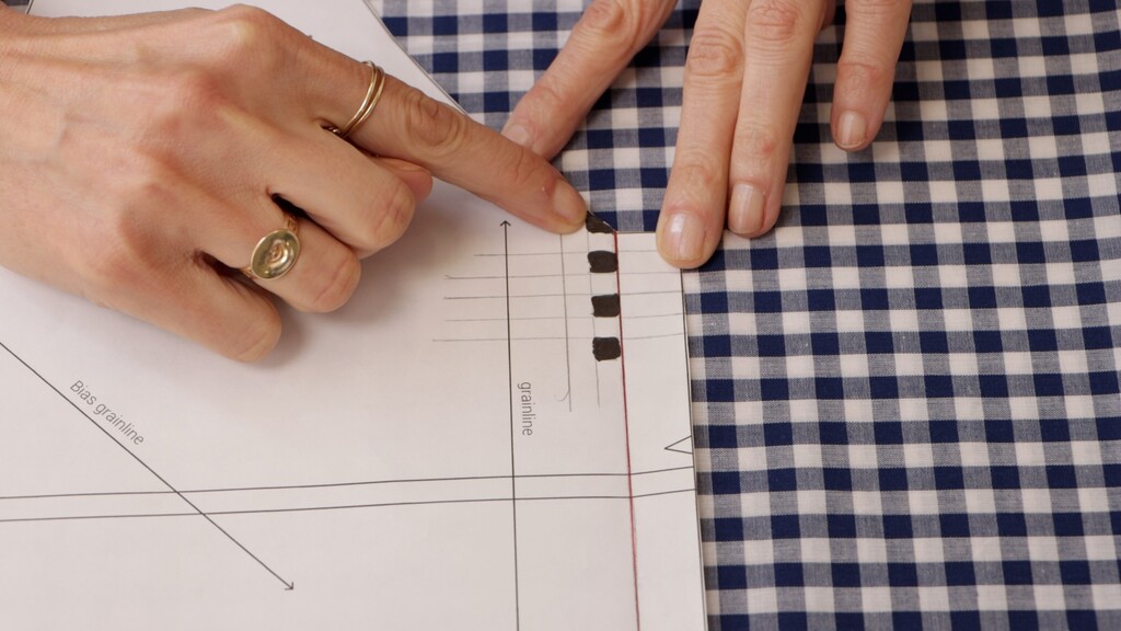 Flat lay of a pattern piece with the seamline drawn in, placed on gingham fabric showing how the seamline aligns to the check rather than the cut edge