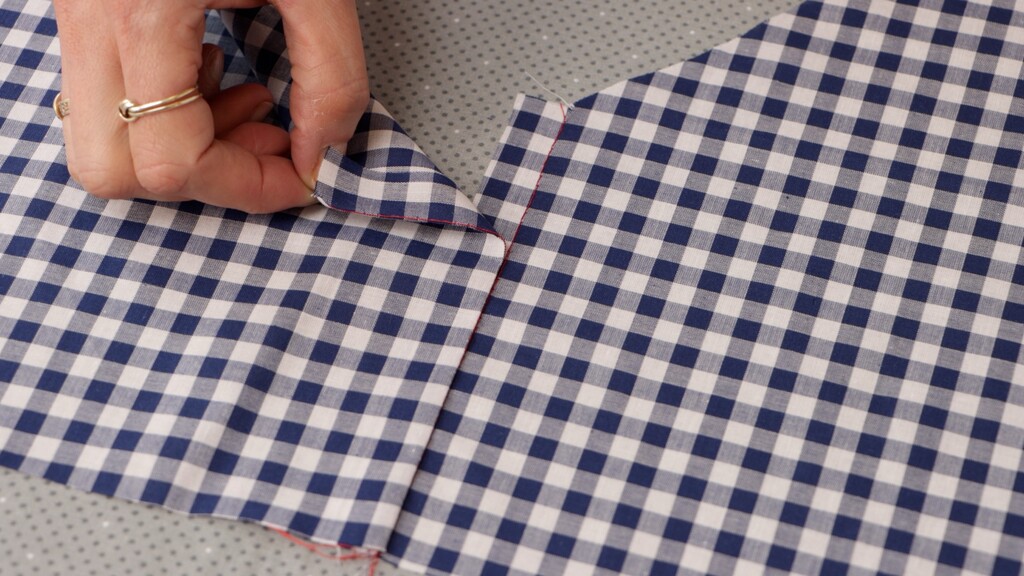 Close-up of the lap-and-edgestitch technique in progress, showing the folded edge lapped over the matching piece with pattern lines visibly aligned, Wonder Tape holding it in place
