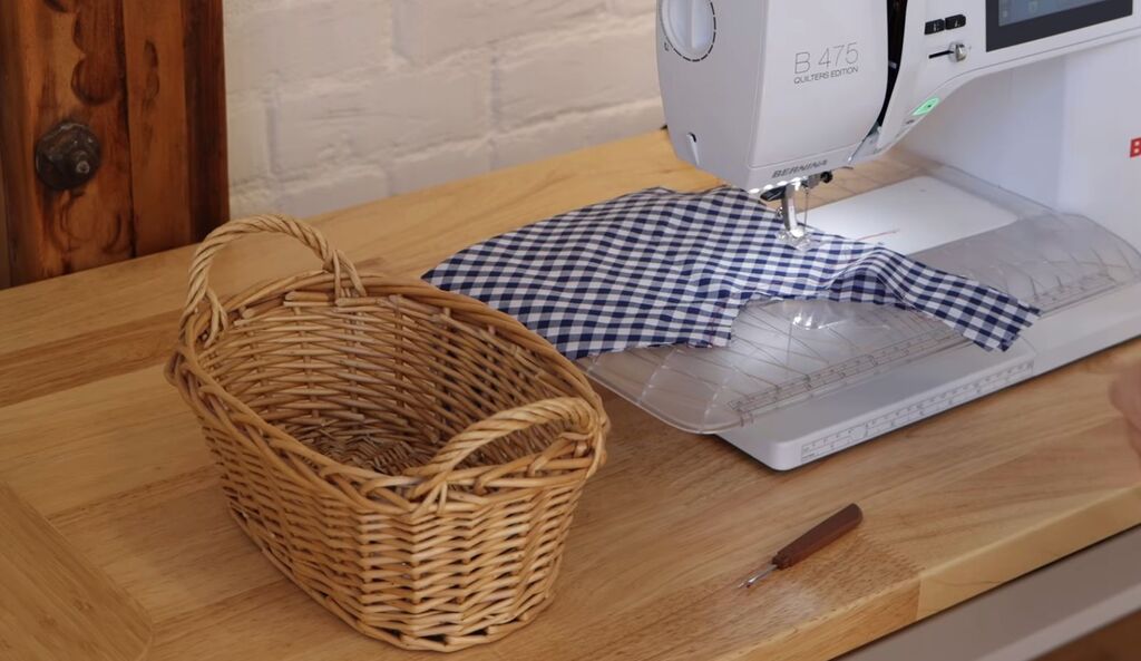 A small basket or tray next to a sewing machine holding a seam ripper, thread snips, and tweezers