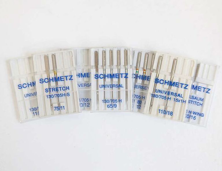 Close-up of several types of sewing machine needles — universal, ballpoint, and denim — in their packaging