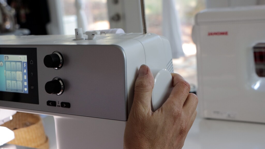 Hands turning a sewing machine hand wheel slowly to guide topstitching around a corner