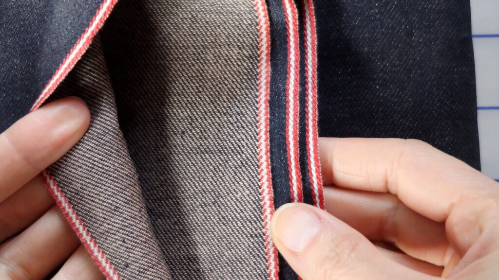 Close-up of raw Japanese selvage denim showing the red selvage line along the fabric edge